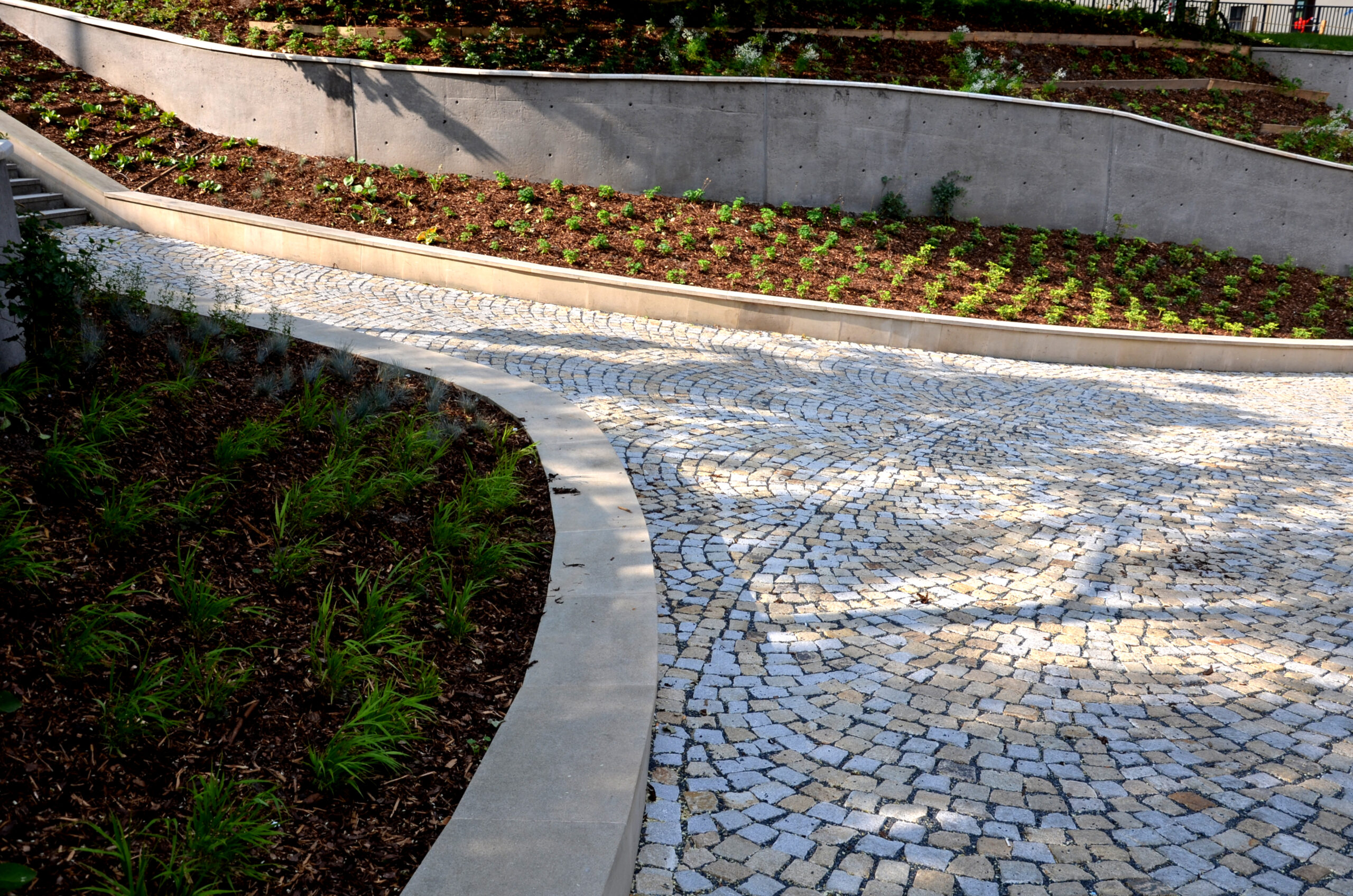 new plantings of perennials in the sloping park with anti-erosion battening. retaining walls cast from concrete in graceful arches. staircase with central railing metal steel, silver